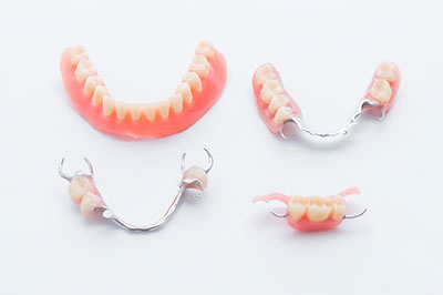The image shows a set of dentures with visible teeth, displayed on a white surface against a neutral background.